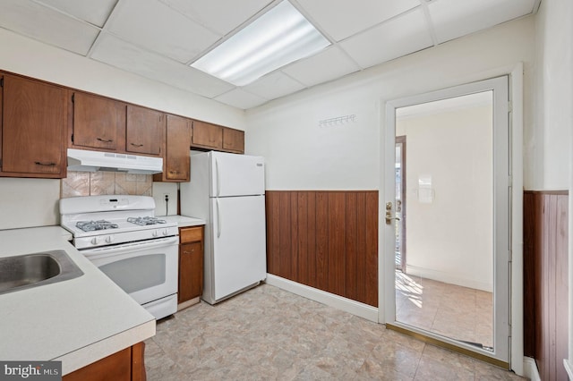 kitchen featuring white appliances, a drop ceiling, light countertops, and under cabinet range hood