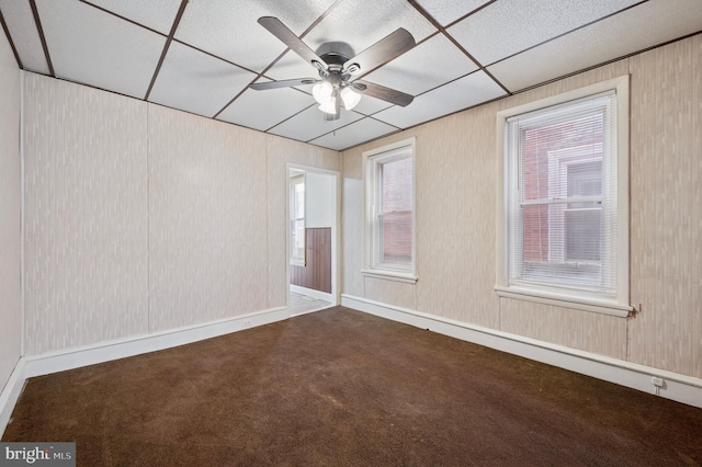 carpeted spare room with a drop ceiling and a ceiling fan