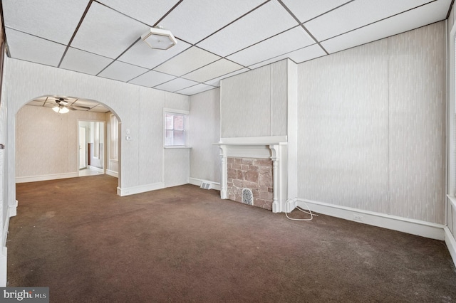 unfurnished living room with a fireplace, carpet, a paneled ceiling, and arched walkways