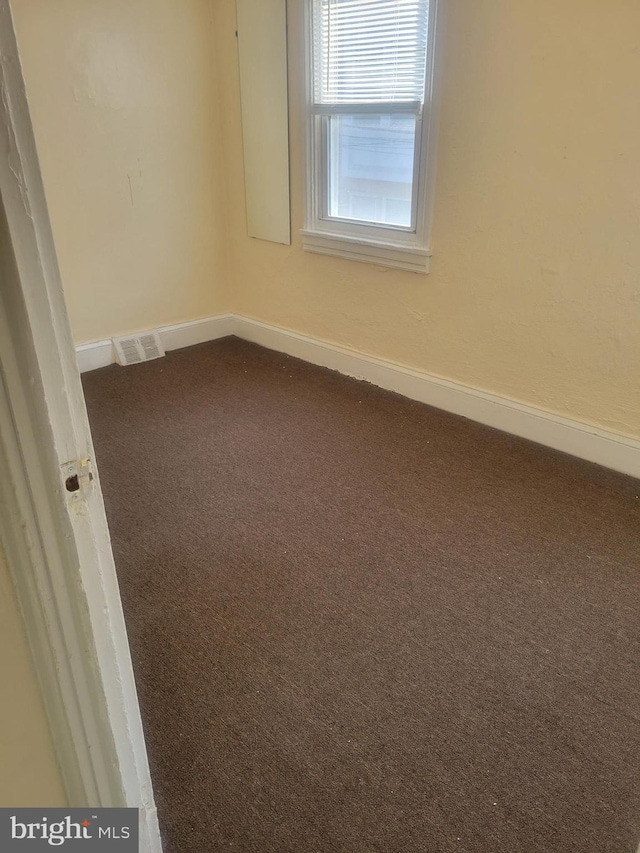 empty room featuring dark colored carpet, visible vents, and baseboards