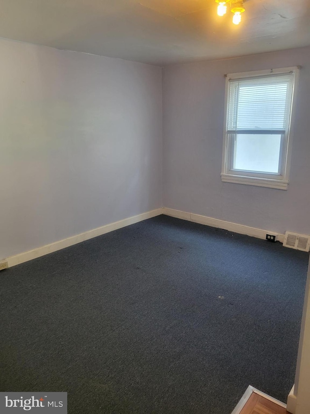 spare room featuring dark colored carpet, visible vents, and baseboards