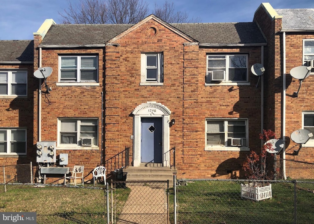 view of property featuring brick siding, a fenced front yard, cooling unit, and a gate