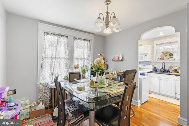 dining area with arched walkways, light wood-style floors, and an inviting chandelier