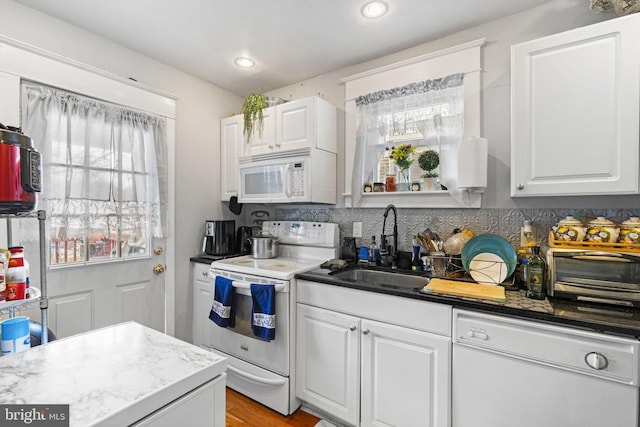 kitchen featuring white appliances, recessed lighting, a sink, white cabinets, and backsplash