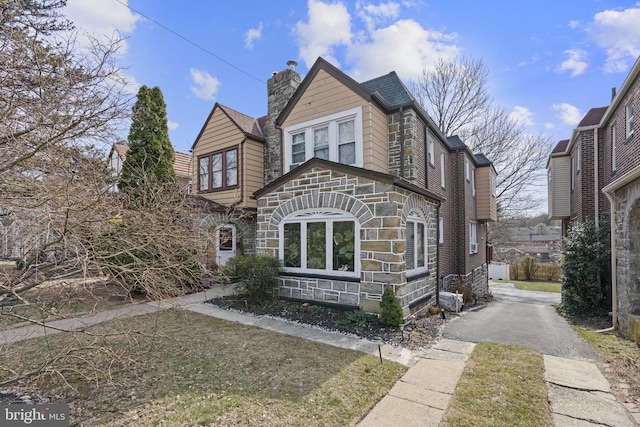 view of front of home featuring stone siding, driveway, and a chimney