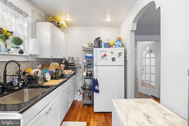 kitchen featuring dark stone countertops, wood finished floors, arched walkways, freestanding refrigerator, and a sink