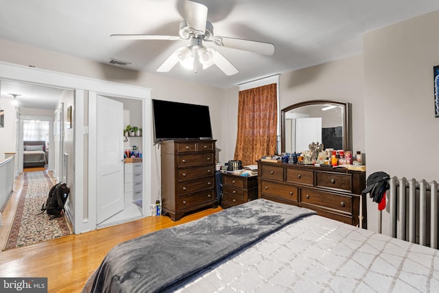 bedroom featuring visible vents, radiator, wood finished floors, and a ceiling fan