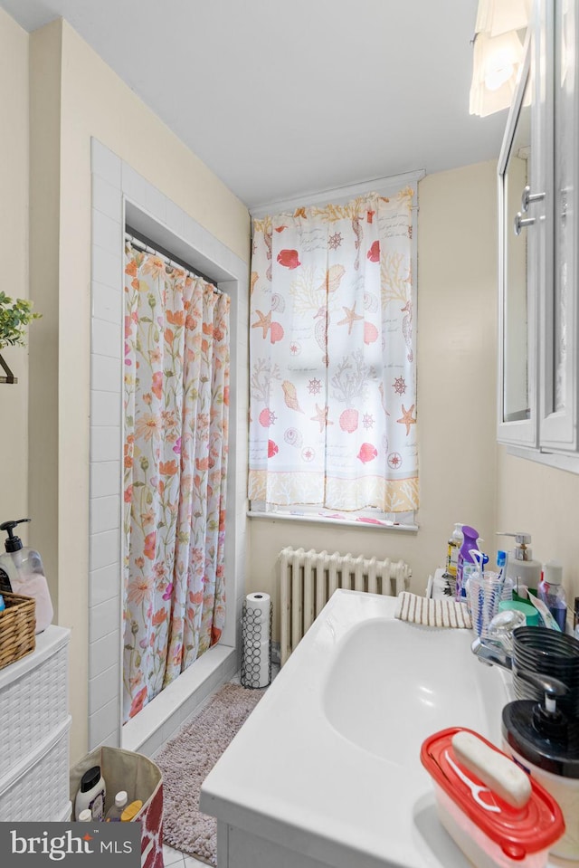 full bathroom featuring a shower with shower curtain, radiator heating unit, and a sink