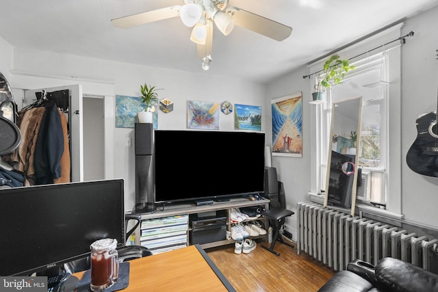 living area with radiator, wood finished floors, and a ceiling fan