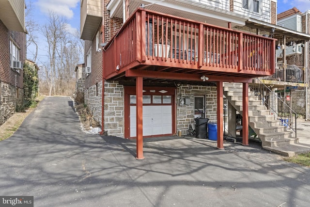 rear view of property with stairs, aphalt driveway, a garage, and stone siding