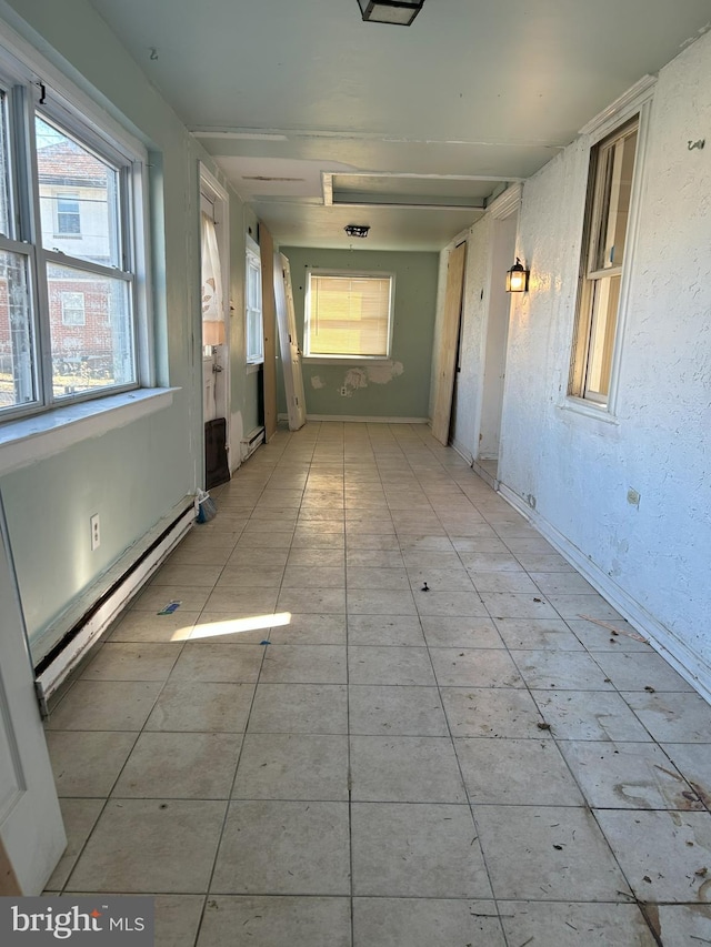 hallway featuring light tile patterned flooring, baseboard heating, and a textured wall