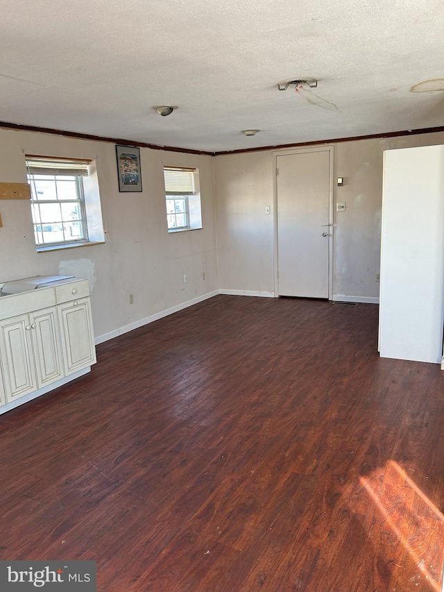 interior space featuring dark wood finished floors, a textured ceiling, baseboards, and ornamental molding