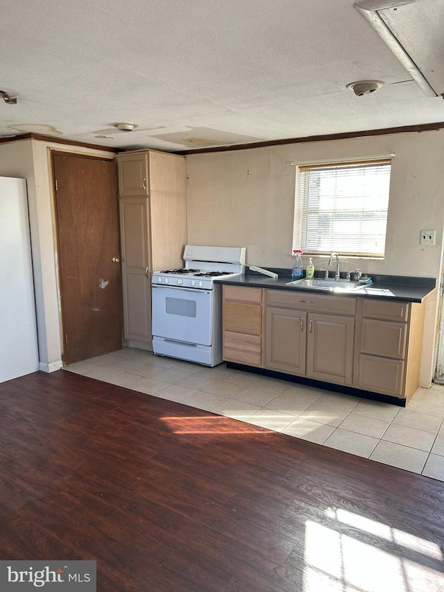 kitchen featuring a sink, dark countertops, a textured ceiling, light wood-style floors, and white range with gas stovetop