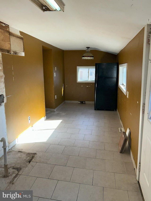 empty room featuring baseboards, a healthy amount of sunlight, light tile patterned flooring, and vaulted ceiling