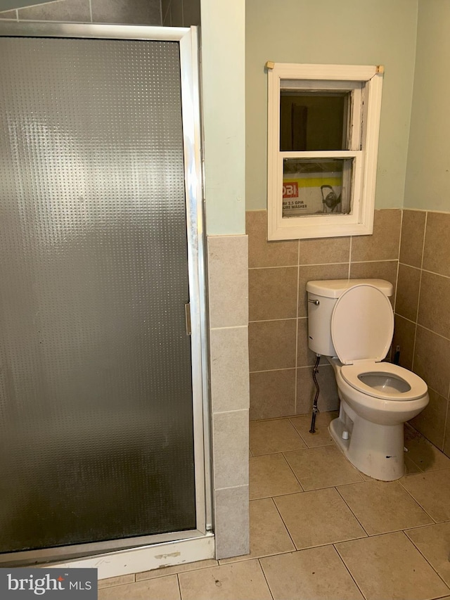 bathroom featuring a stall shower, tile patterned flooring, wainscoting, tile walls, and toilet