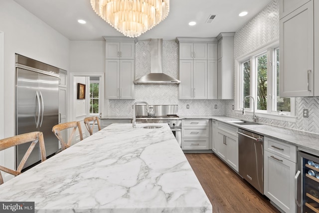 kitchen with high end appliances, dark wood finished floors, a sink, wine cooler, and wall chimney exhaust hood