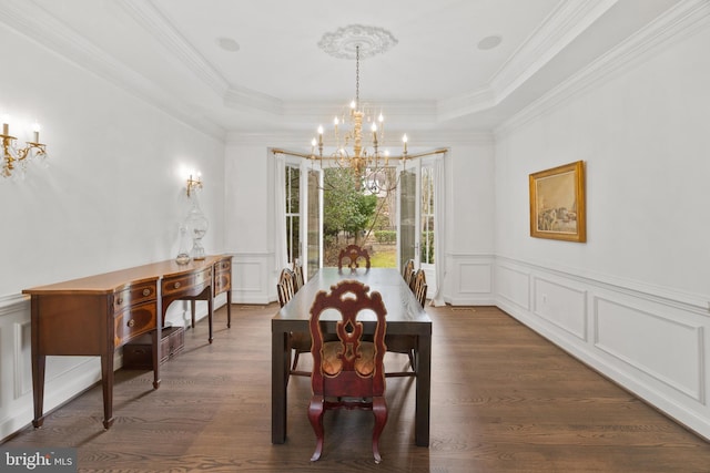 dining space with ornamental molding, a notable chandelier, a decorative wall, a raised ceiling, and dark wood-style flooring