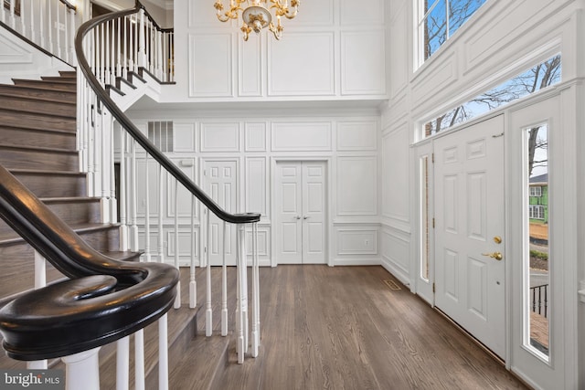 entryway featuring a notable chandelier, stairs, a towering ceiling, dark wood-style floors, and a decorative wall