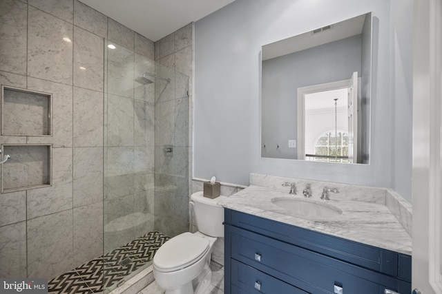 bathroom with visible vents, toilet, vanity, and a tile shower