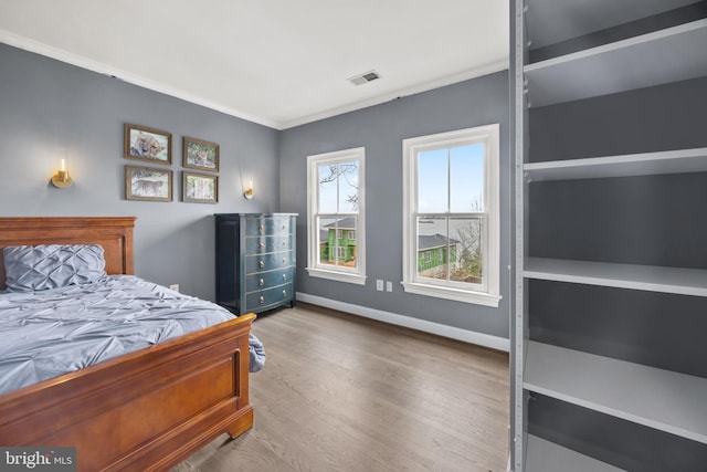 bedroom featuring ornamental molding, wood finished floors, visible vents, and baseboards