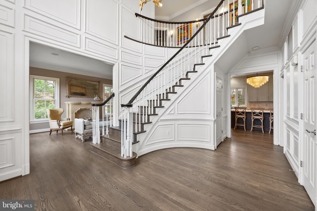 entryway with stairway, a notable chandelier, ornamental molding, and dark wood finished floors