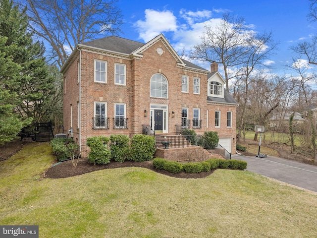 view of front of home with an attached garage, a chimney, a front lawn, aphalt driveway, and brick siding