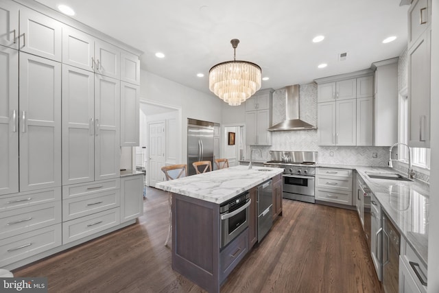 kitchen featuring dark wood finished floors, premium appliances, decorative backsplash, wall chimney exhaust hood, and a sink