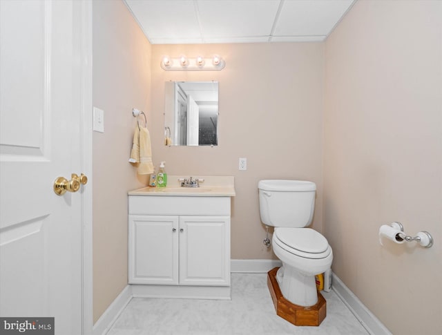 bathroom featuring toilet, baseboards, a drop ceiling, and vanity