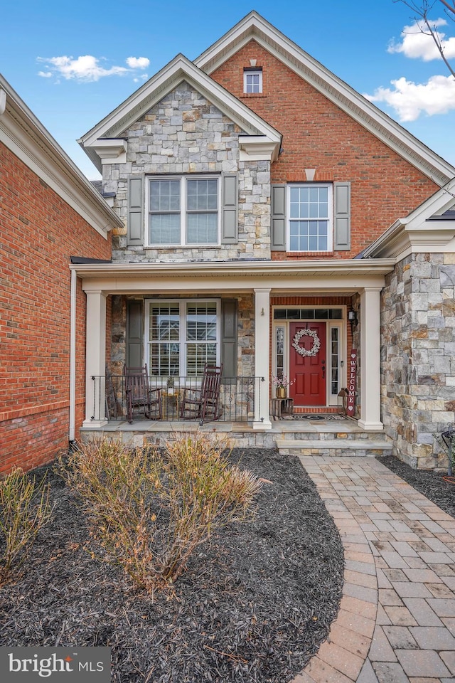 view of front of home with brick siding, covered porch, and stone siding