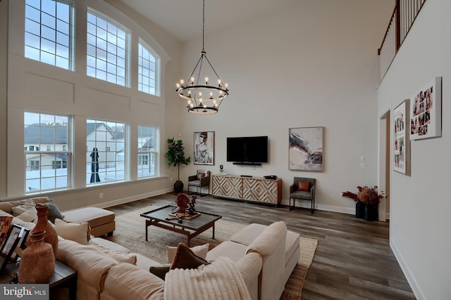 living area with dark wood-style floors, baseboards, a towering ceiling, and an inviting chandelier