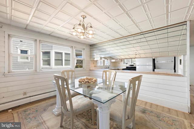 dining area with baseboard heating, wood finished floors, wood walls, and an ornate ceiling