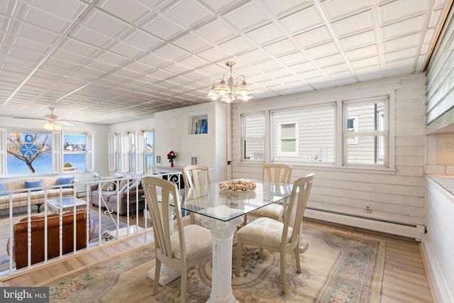 dining space featuring a baseboard heating unit, plenty of natural light, wood finished floors, and wood walls