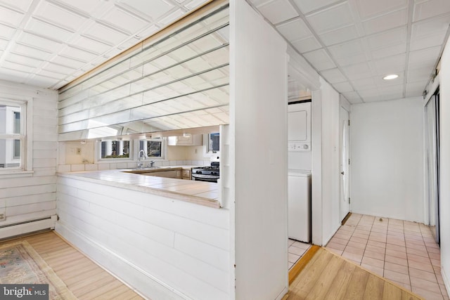 kitchen featuring a sink, stacked washing maching and dryer, light wood finished floors, gas range, and tile counters