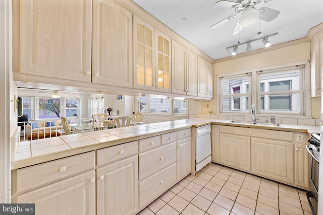 kitchen featuring tile countertops, a ceiling fan, white dishwasher, a sink, and gas range