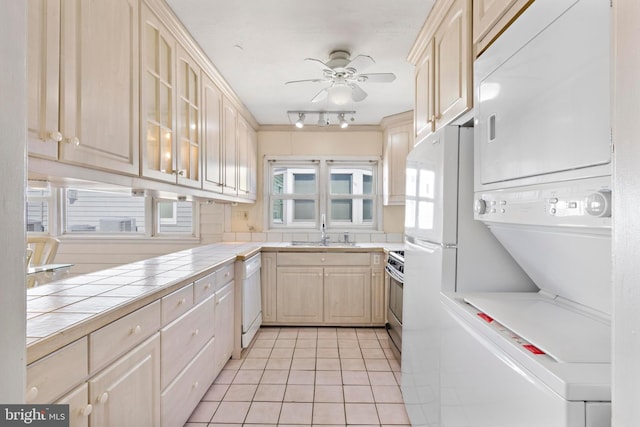 kitchen with tile countertops, dishwasher, stainless steel range, stacked washer / drying machine, and a sink