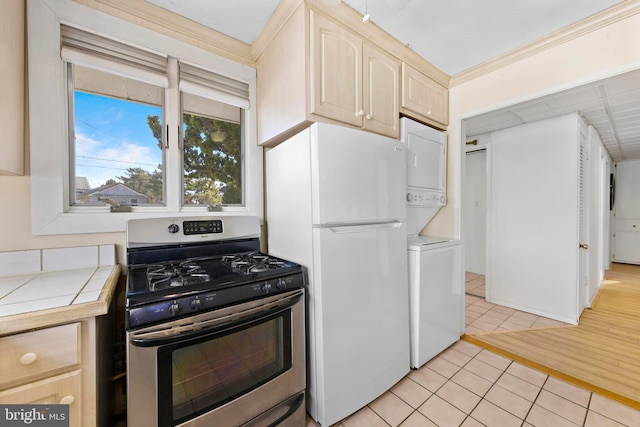 kitchen featuring stainless steel gas range, freestanding refrigerator, light brown cabinetry, tile counters, and stacked washer and clothes dryer