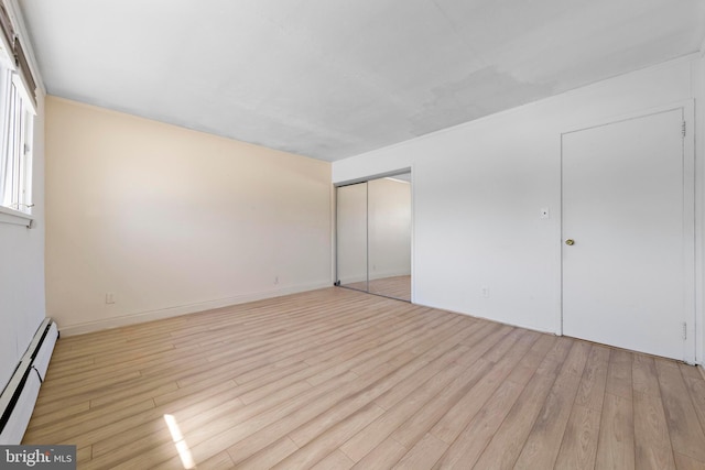 unfurnished bedroom featuring a closet, baseboard heating, and light wood-style flooring