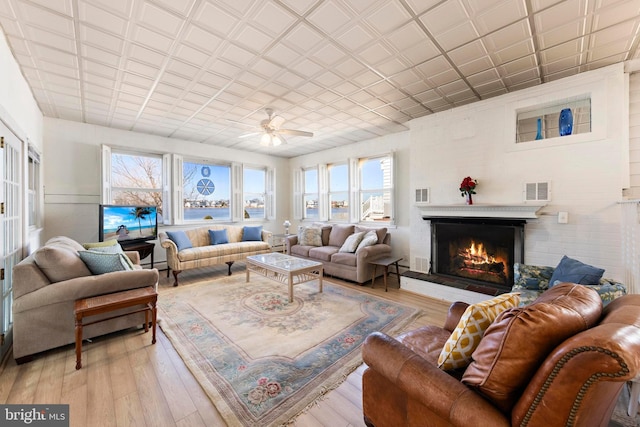 living area featuring visible vents, an ornate ceiling, a brick fireplace, and light wood finished floors