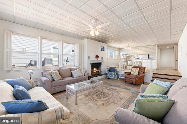 living room with a ceiling fan, wood finished floors, and a lit fireplace