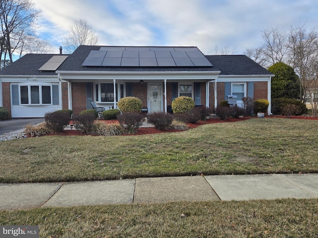 view of front of property with covered porch, a front yard, solar panels, and brick siding