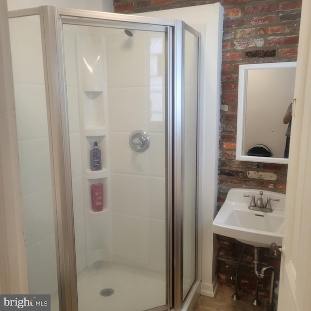 bathroom featuring a sink, brick wall, and a shower stall