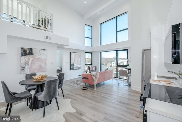 dining area featuring light wood-style floors, visible vents, a towering ceiling, and baseboards