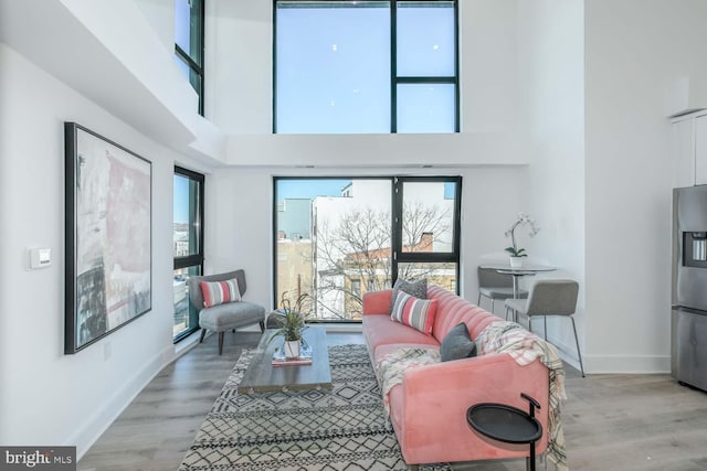 living area with light wood finished floors, a towering ceiling, and baseboards