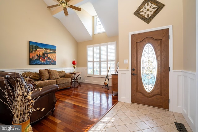 foyer entrance featuring a ceiling fan, a wainscoted wall, visible vents, high vaulted ceiling, and hardwood / wood-style flooring