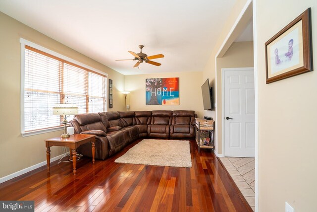 living area with baseboards, dark wood-type flooring, and a ceiling fan