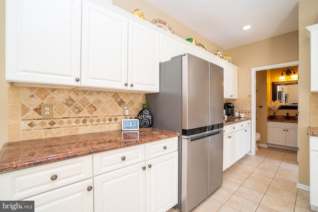 kitchen with backsplash, dark stone counters, light tile patterned floors, freestanding refrigerator, and white cabinets