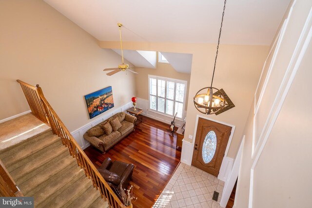 foyer entrance featuring vaulted ceiling, ceiling fan with notable chandelier, stairs, and wood finished floors