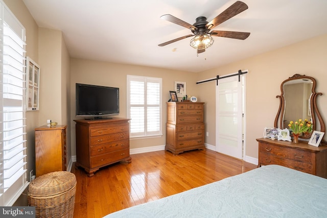 bedroom with ceiling fan, baseboards, a barn door, and hardwood / wood-style floors