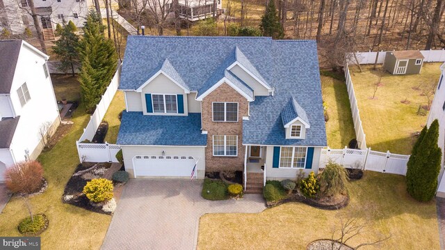 view of front facade with roof with shingles, decorative driveway, a fenced backyard, an attached garage, and a gate