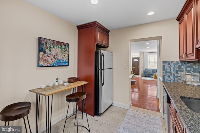 kitchen with tasteful backsplash, baseboards, dark stone counters, appliances with stainless steel finishes, and light tile patterned flooring